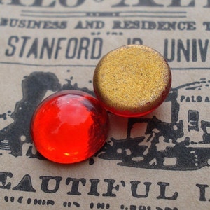 May include: Two round glass paperweights. One is red and the other is gold.
