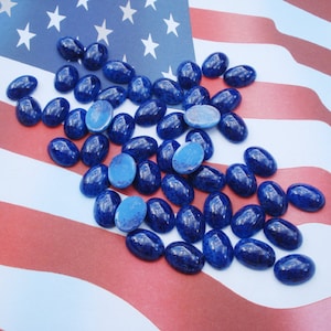 May include: A collection of oval-shaped, blue, speckled cabochons, scattered on a red, white, and blue American flag.