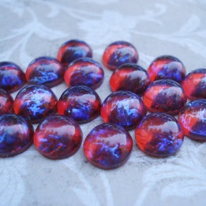 May include: A collection of 15 round, iridescent glass cabochons with a red and blue marbled pattern. The cabochons are approximately 1 inch in diameter.