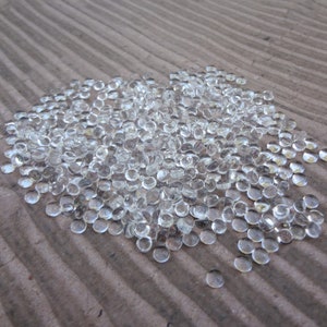May include: A large pile of clear glass beads, scattered on a brown textured surface.