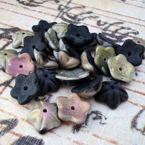 May include: A collection of 20 flower-shaped glass beads in black, iridescent green, and iridescent pink. The beads have a five-pointed star shape and a hole in the center for stringing.