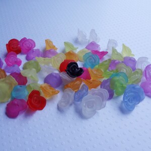 May include: Assortment of colorful translucent plastic rose-shaped beads. The beads are in various shades of pink, purple, blue, green, yellow, orange, and red. One bead is black.