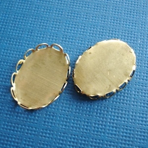 Puede incluir: Dos engastes ovalados de metal de color dorado con un borde festoneado decorativo. Los engastes est&aacute;n dise&ntilde;ados para sujetar un cabuj&oacute;n u otra piedra de fondo plano.