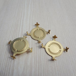 以下が含まれることがあります： 丸い中心と4本の装飾的な腕を持つ、金色の金属製の装飾的な装飾品が3つあります。各装飾品は、中心の円周に沿って隆起したビーズ状のエッジを持っています。