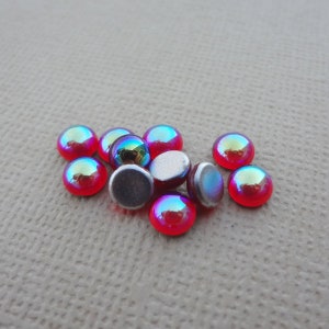 May include: A group of iridescent red and silver round cabochons. The cabochons are about 1/2 inch in diameter and have a smooth, shiny surface.