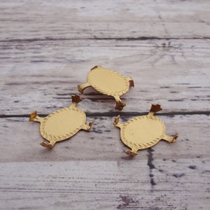 May include: Three gold-colored metal turtle-shaped settings for a jewelry display.
