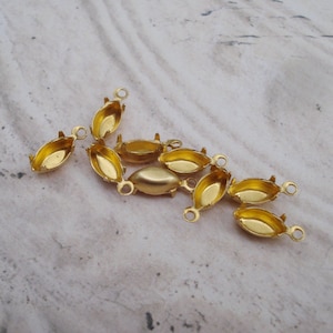 May include: A group of eight gold-toned metal oval-shaped settings for cabochon stones. The settings have a loop at the top for attaching to jewelry.