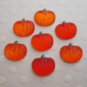 May include: Seven orange glass pumpkin shaped ornaments with a carved jack-o'-lantern face. The ornaments have a green stem.
