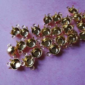 May include: A group of gold-toned metal bead caps with three loops on each. The bead caps are scattered on a pink surface.