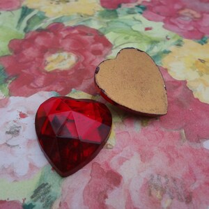 May include: Two heart-shaped embellishments, one red and one gold. The red heart is faceted and has a shiny finish. The gold heart is flat and has a matte finish.