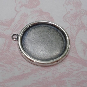 May include: Silver-toned round pendant with a smooth, slightly textured surface. The pendant has a loop at the top for attaching to a chain or cord.