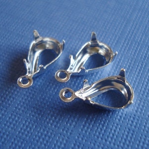 May include: Three silver-toned earring bails with a teardrop shape and a small loop at the top. The bails are designed to hold a gemstone or other embellishment.