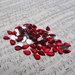 May include: A large pile of red teardrop-shaped rhinestones on a sheet of music.