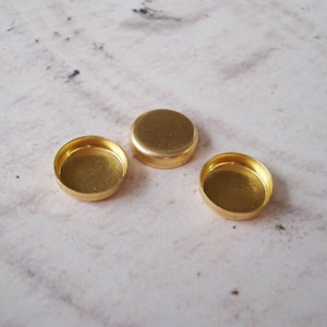 May include: Three gold-colored metal round containers with a smooth, shiny finish. The containers are slightly raised on the edges and have a flat bottom.