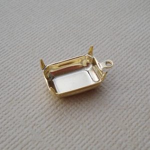 May include: Gold-toned metal setting for a square-shaped cabochon stone. The setting has four prongs and a loop for attaching a chain or cord.