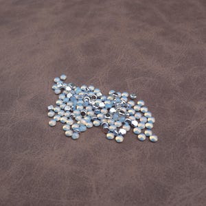 May include: A pile of small, round, iridescent white rhinestones with silver backs.