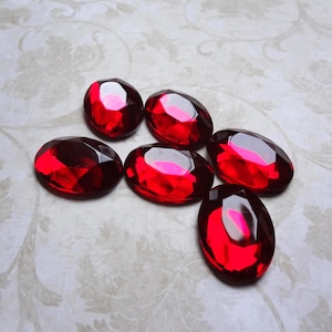Peut inclure: Six pierres précieuses rouges de forme ovale et à facettes avec une finition polie. Chaque pierre présente une teinte cramoisie profonde et brillante ainsi qu'une surface à facettes qui reflète la lumière, créant des reflets distincts.