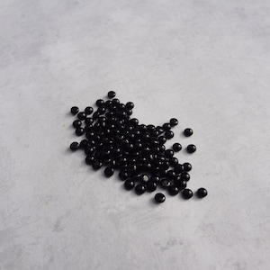 May include: A pile of small, black, round beads on a light gray surface.
