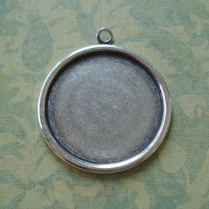 May include: Silver-toned round pendant with a smooth, slightly textured surface. The pendant has a loop at the top for attaching a chain or cord.