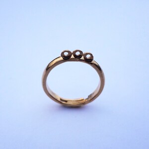 May include: A gold ring with three round openings on the top. The ring is adjustable and has a smooth finish.