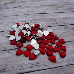 May include: A pile of red and silver heart-shaped embellishments. The hearts are made of glass or plastic and have a shiny finish.