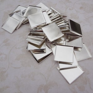 May include: A collection of shiny, silver-colored square metal trays. The trays are arranged in a pile, with some overlapping. The edges of the trays are slightly raised, creating a shallow dish. The trays are likely for crafting or jewelry making.