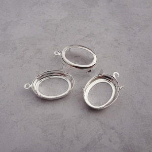 May include: Three silver oval-shaped pendant settings with prongs. The settings are designed to hold a cabochon stone.