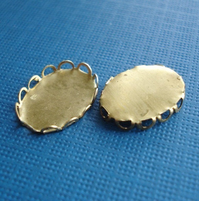 Puede incluir: Dos engastes ovalados de metal de color dorado con un borde festoneado decorativo. Los engastes son para hacer joyas o manualidades.