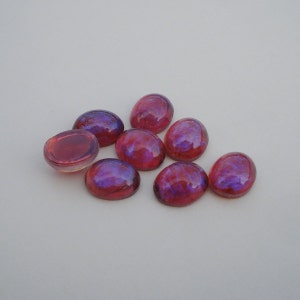 May include: Eight iridescent oval-shaped glass cabochons in shades of pink and purple. The cabochons are arranged in a loose cluster on a white background.