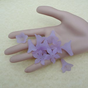 May include: A collection of lavender-colored plastic flower beads. The beads are shaped like flowers with five petals and are translucent.