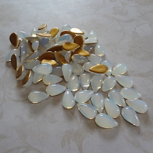 May include: A large pile of white teardrop-shaped glass beads with a few gold teardrop-shaped beads mixed in.