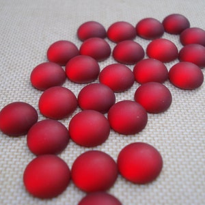 May include: A group of 20 red glass cabochons, arranged in a semi-circle pattern. The cabochons are smooth and have a slightly frosted finish.
