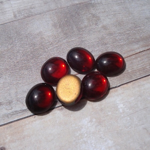 May include: Six red glass cabochons, oval shaped, with a gold cabochon in the center.