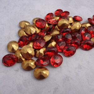 May include: A pile of red and gold glass rhinestones. The rhinestones are scattered on a light gray surface.