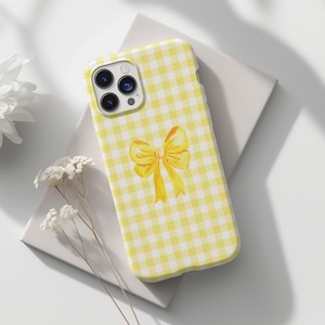 May include: A yellow and white gingham phone case with a yellow bow in the centre.
