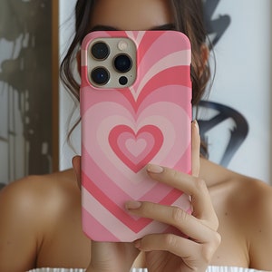 May include: A pink and white phone case with a heart design. The case has a raised heart design with concentric circles of pink and white.
