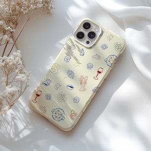 May include: A white phone case with a pattern of red, blue, and yellow illustrations of food, wine glasses, and seashells. The phone case has a camera lens cutout and a white background.