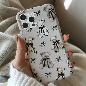 Könnte beinhalten: Eine weiße iPhone-Hülle mit einem sich wiederholenden Muster aus Teddybären in Schwarzweiß. Die Bären sind in verschiedenen Posen dargestellt und haben eine aquarellartige Optik.