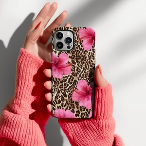 May include: A phone case featuring a leopard print and pink hibiscus flowers. The case is made from hard plastic and has a matte finish.