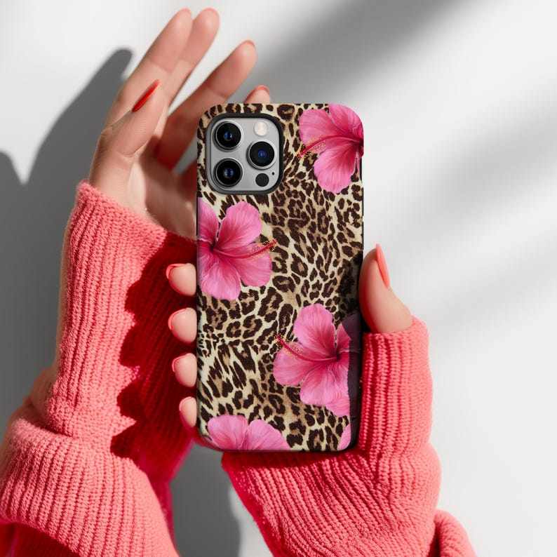 May include: A phone case featuring a leopard print and pink hibiscus flowers. The case is made from hard plastic and has a matte finish.