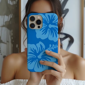 Op de afbeelding: Een blauwe telefoonhoes met een wit hibiscusbloemdessin. De hoes heeft een uitsparing voor de cameralens en een verhoogde rand rond de randen.