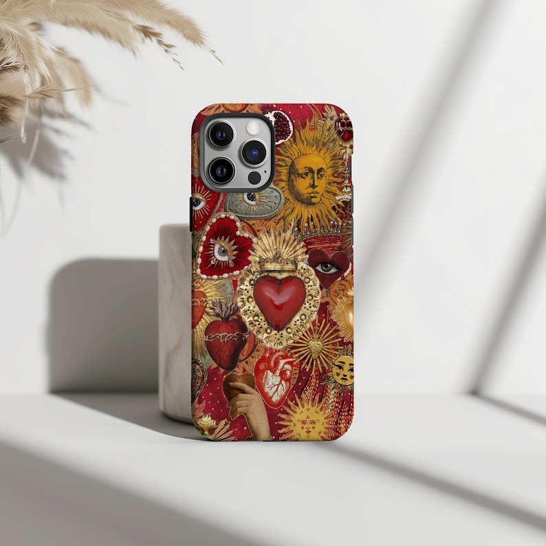 May include: A red, gold and white iPhone case featuring a collage of hearts, suns and eyes. The case has a vintage, ornate design.