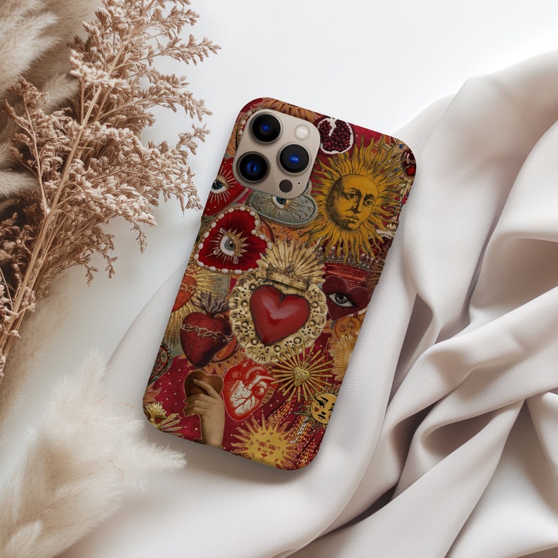 May include: A red, gold and white iPhone case featuring a collage of hearts, eyes and suns. The case has a vintage aesthetic and features a large red heart with a crown.