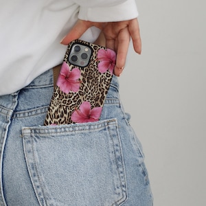 May include: A black phone case with a leopard print and pink hibiscus flowers. The case is in a back pocket of blue jeans.