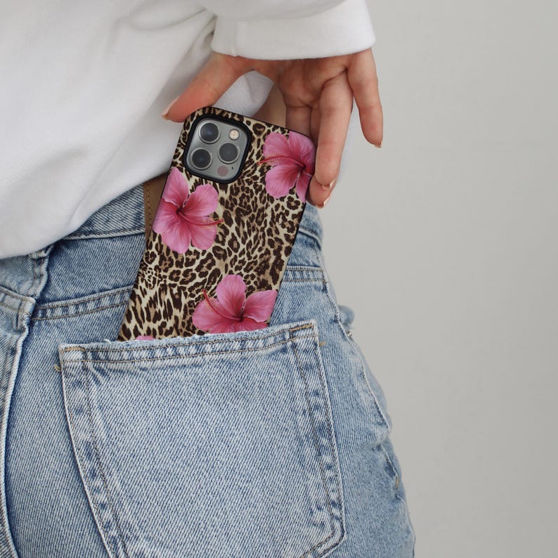 May include: A black phone case with a leopard print and pink hibiscus flowers. The case is in a back pocket of blue jeans.