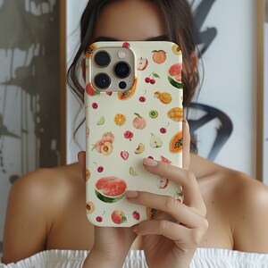 May include: A white phone case with a colorful fruit pattern. The case features a variety of fruits, including watermelon, pineapple, papaya, and strawberries. The case is designed for a phone with a triple camera lens.