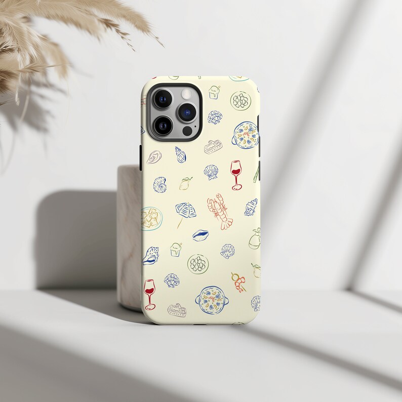 May include: A white iPhone case with a pattern of various food items, including pasta, wine glasses, and seafood. The case has a camera cutout and a cream background.
