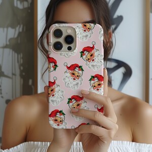 May include: A pink phone case featuring a repeating pattern of vintage Santa Claus faces with red hats and white beards. The case has a glossy finish and a camera cutout.