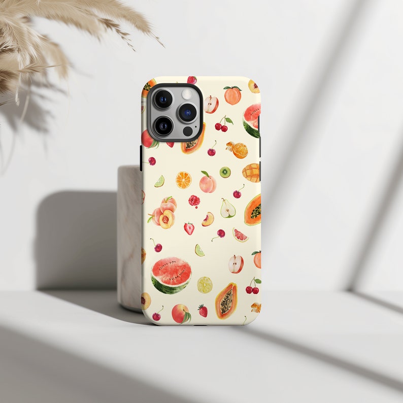 May include: A white iPhone case with a colorful fruit pattern. The pattern includes watermelon, peaches, strawberries, cherries, papaya, pineapple, and lemons.