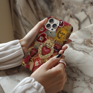May include: A red, gold and white iPhone case featuring a collage of religious imagery, including hearts, eyes and a sun with a face. The case has a camera lens cutout.